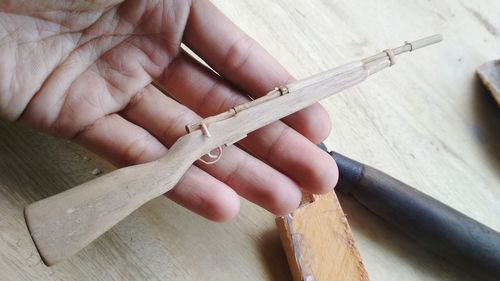 Cropped hand holding small wooden gun on table