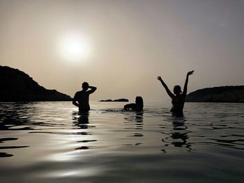 Silhouette people in sea against sky during sunset