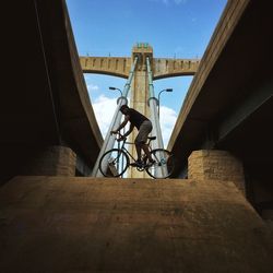 Low angle view of man balancing on bicycle along bridge