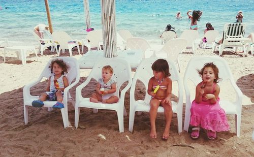 Full length portrait of children sitting on chair at beach