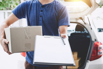 Midsection of messenger holding blank paper in clipboard outdoors