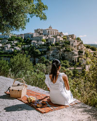 Rear view of woman sitting on building against sky