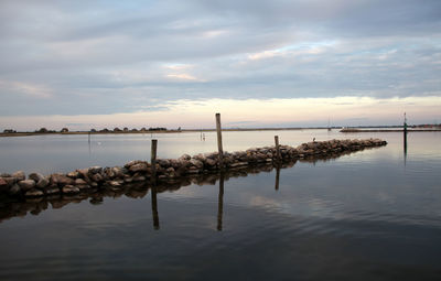 Wooden posts in sea against sky during sunset