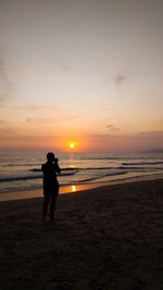 Silhouette man standing on beach against sky during sunset