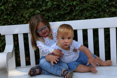 Siblings sitting on bench against plants