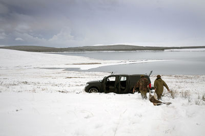 Rear view of hunters pulling on red deer on snowcapped field