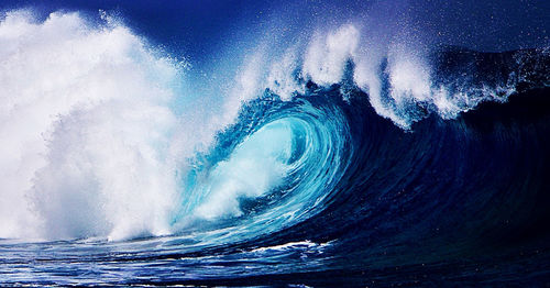 Waves splashing on shore against blue sky