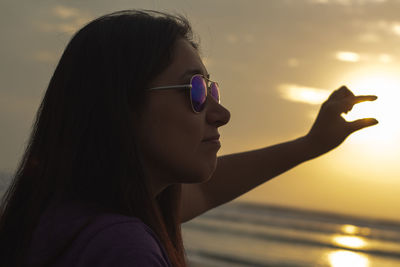 Close-up portrait of young woman wearing sunglasses against sky during sunset