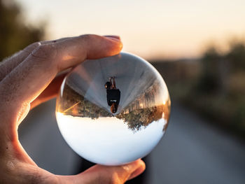 Close-up of hand holding crystal ball against sky at sunset