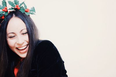 Close-up of happy young woman wearing wreath against white background