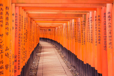 Footpath amidst orange torii gates with chinese script