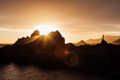 Sunlight streaming through mountains against sky during sunset