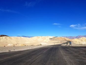 Scenic view of road on desert against blue sky