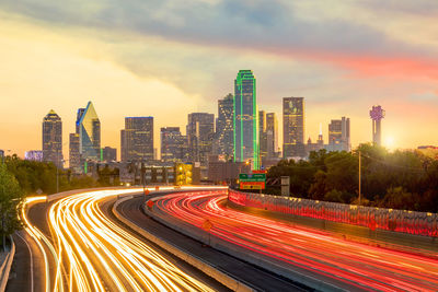 Light trails on road by buildings against sky in city