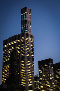 Low angle view of illuminated skyscrapers against clear blue sky at night