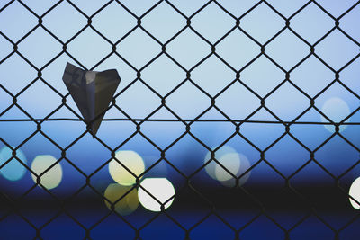 Paper airplane on chainlink fence against sky
