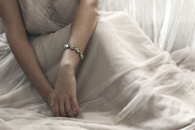 Low section of bride in dress sitting on bed at home