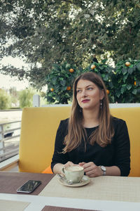 Young woman looking away while sitting on table
