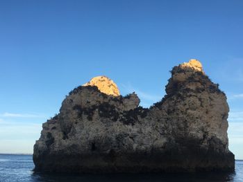 Rock formation by sea against clear blue sky