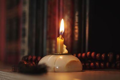 Close-up of lit candle and books on shelf