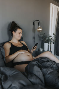 Pregnant woman relaxing in bed and using phone