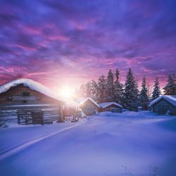 Snow covered houses and buildings against sky during sunset