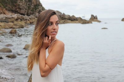 Young caucasian blonde girl in white dress pensive in the sea with cloudy sky