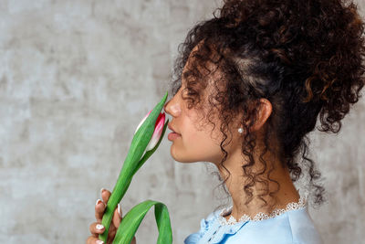 Young woman holding tulip while standing against wall