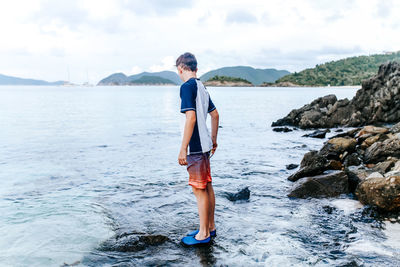 Full length of man standing on rock at sea shore against sky