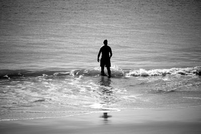 Silhouette man standing in waves at shore