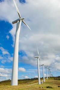 Low angle view of windmills on field against sky