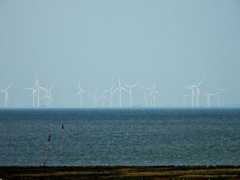 Wind turbines by sea against sky