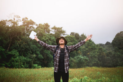 Young man standing with arms outstretched on field against sky