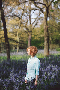 Woman standing amidst purple flowering plants at forest