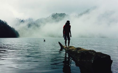 Man standing on log over ranu kumbolo lake during foggy weather