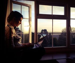 Woman using laptop while sitting on window sill