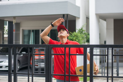 Delivery man standing at closed gate against buildings