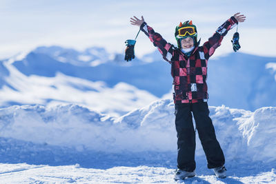 Portrait of happy boy with arms outstretched standing against snowcapped mountains