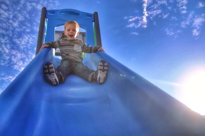 Portrait of a cute little boy on slide against blue sky