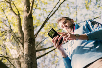 Low angle view of man using mobile phone while standing by tree