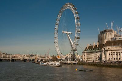 Ferris wheel by river against sky in city