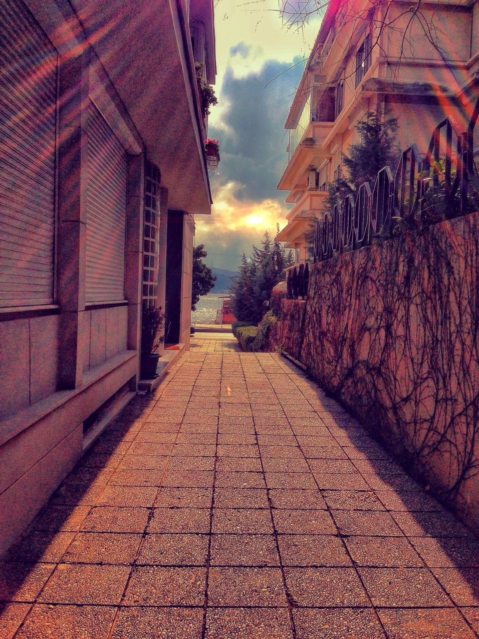 architecture, building exterior, built structure, the way forward, cobblestone, sky, street, sunset, diminishing perspective, vanishing point, narrow, residential structure, cloud - sky, house, footpath, town, city, walkway, residential building, building