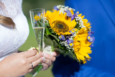 Midsection of bride holding champagne flute and bouquet