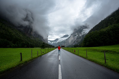 Rear view of man standing on road amidst mountains against sky
