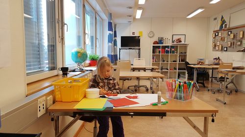 Cute girl making craft while sitting at table in classroom