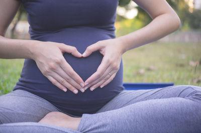 Low section of pregnant woman meditating at park