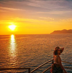 Woman standing on sea against sky during sunset