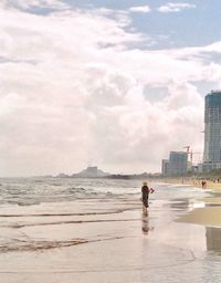 Man standing on beach against cloudy sky