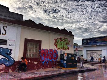 Graffiti on wall in front of building against cloudy sky