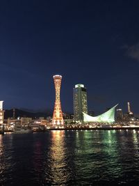 Illuminated bridge over river by buildings against sky at night